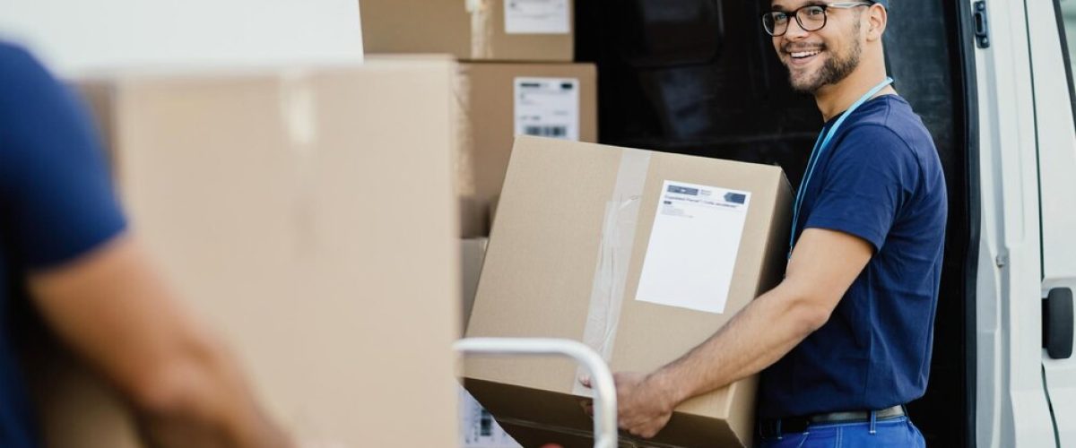 young-happy-manual-worker-carrying-cardboard-boxes-delivery-van-while-communicating-with-his-colleagues_637285-1260